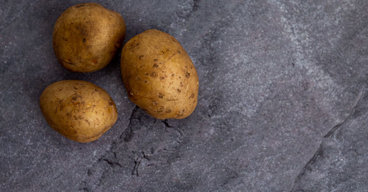Trois pommes de terre entières posées sur une surface en pierre grise foncée.