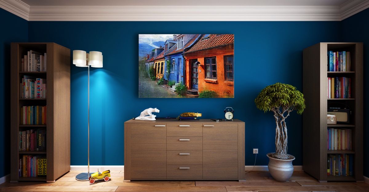 Meuble en bois bas placé contre un mur bleu, sous un cadre décoratif, entre deux bibliothèques dans un salon.