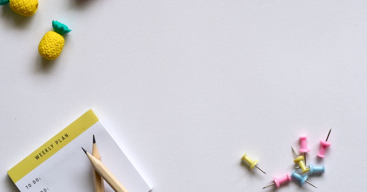 Un bloc-notes intitulé « Weekly Plan » avec un crayon, entouré de petites gommes en forme d'ananas et de punaises colorées sur fond blanc.