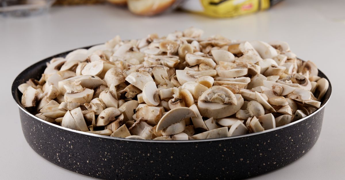 Champignons de Paris coupés en morceaux et entassés dans une poêle noire, prêts à être cuits.