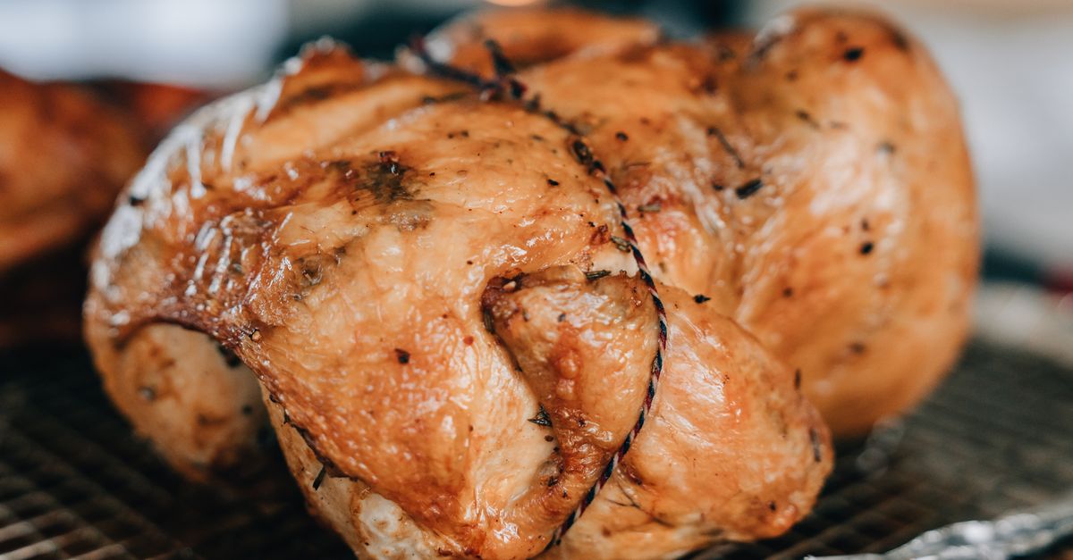 Poulet entier rôti, doré et ficelé, présenté en gros plan sur une grille de four.