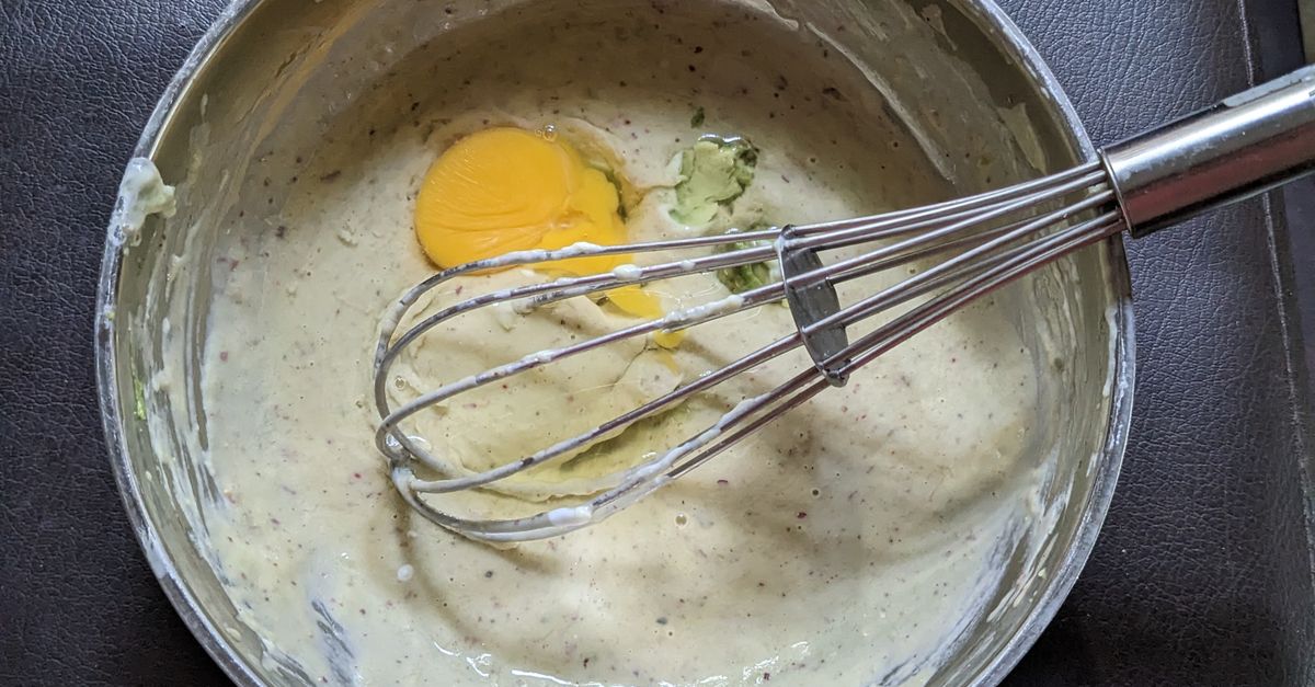 Une sauce crémeuse dans une casserole avec un fouet, mélangée à un jaune d'œuf et des herbes.