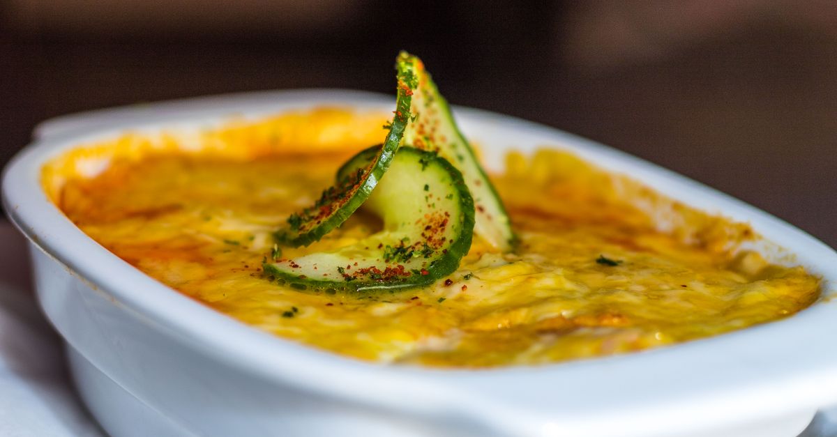 Gratin doré dans un plat blanc, nappé d'une sauce onctueuse et décoré d'une fine tranche de courgette en spirale.