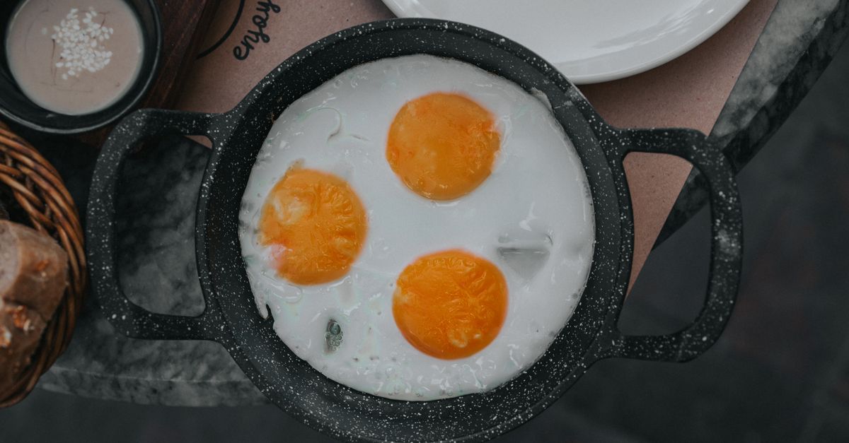 Trois œufs au plat aux jaunes bien ronds cuisant dans une poêle en fonte noire vue de dessus.