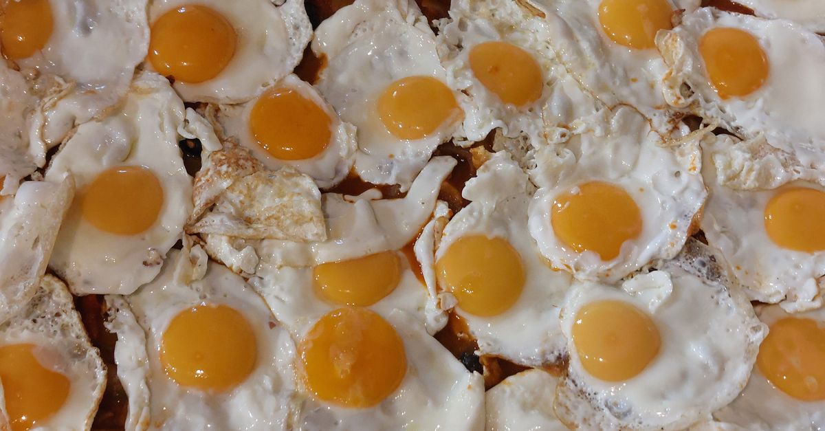 Plusieurs œufs au plat avec des jaunes intacts et coulants disposés en rangées sur une plaque de cuisson.