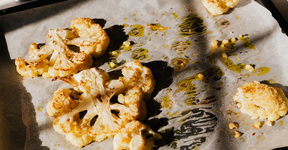 Des morceaux de chou-fleur rôtis aux bords dorés sur une plaque de cuisson recouverte de papier sulfurisé avec des filets d'huile.