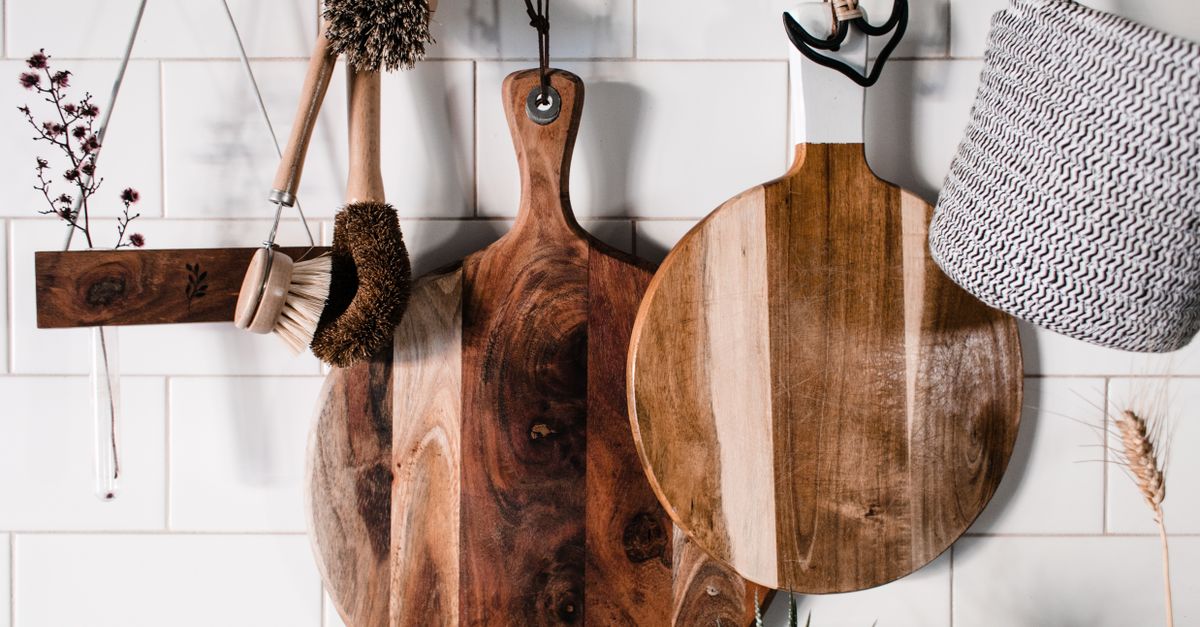 Plusieurs planches à découper en bois suspendues à un mur carrelé blanc, accompagnées de brosses en bois pour le nettoyage.