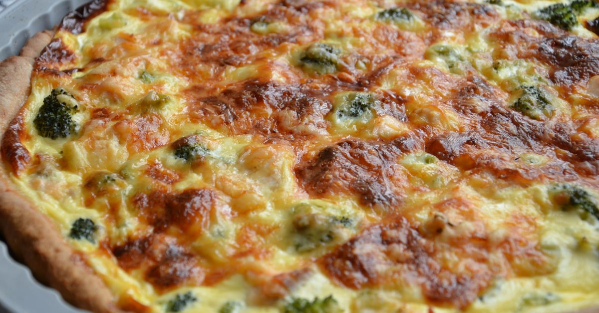 Une tarte salée au fromage et brocolis avec une pâte brisée dorée visible sur les bords du moule.