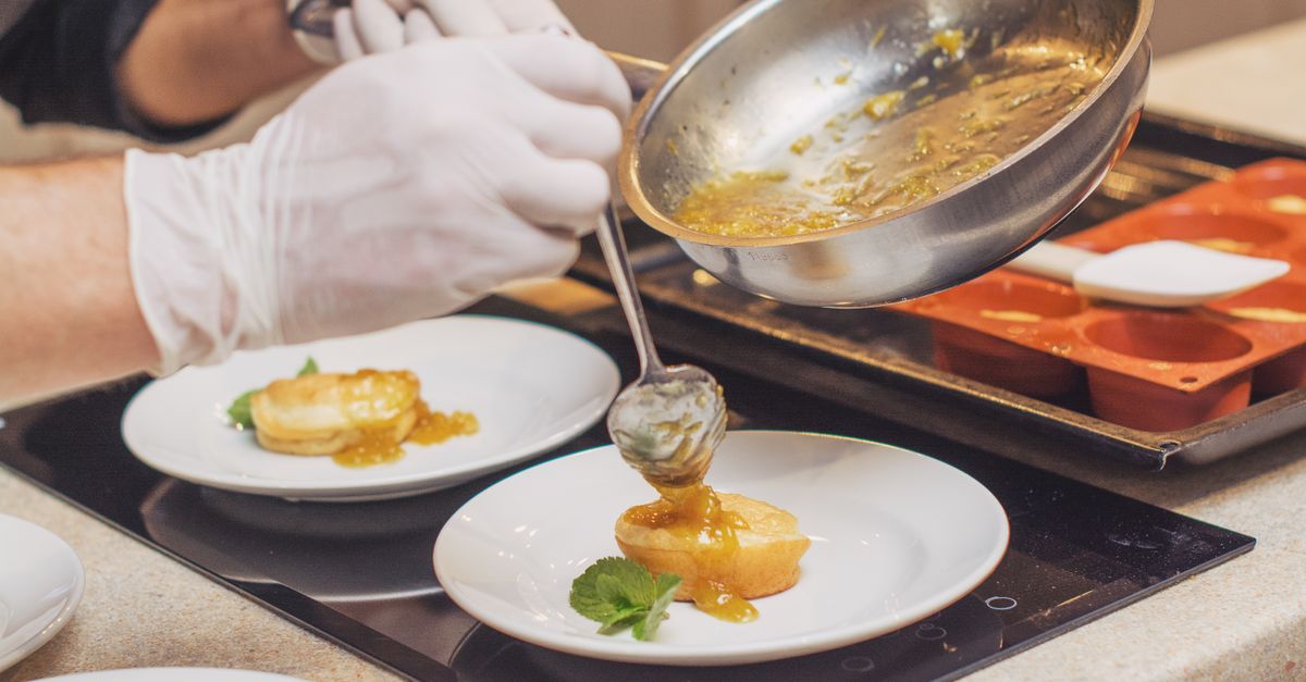 Un chef verse une sauce hollandaise depuis une casserole avec une cuillère sur des œufs pochés disposés sur des assiettes blanches.