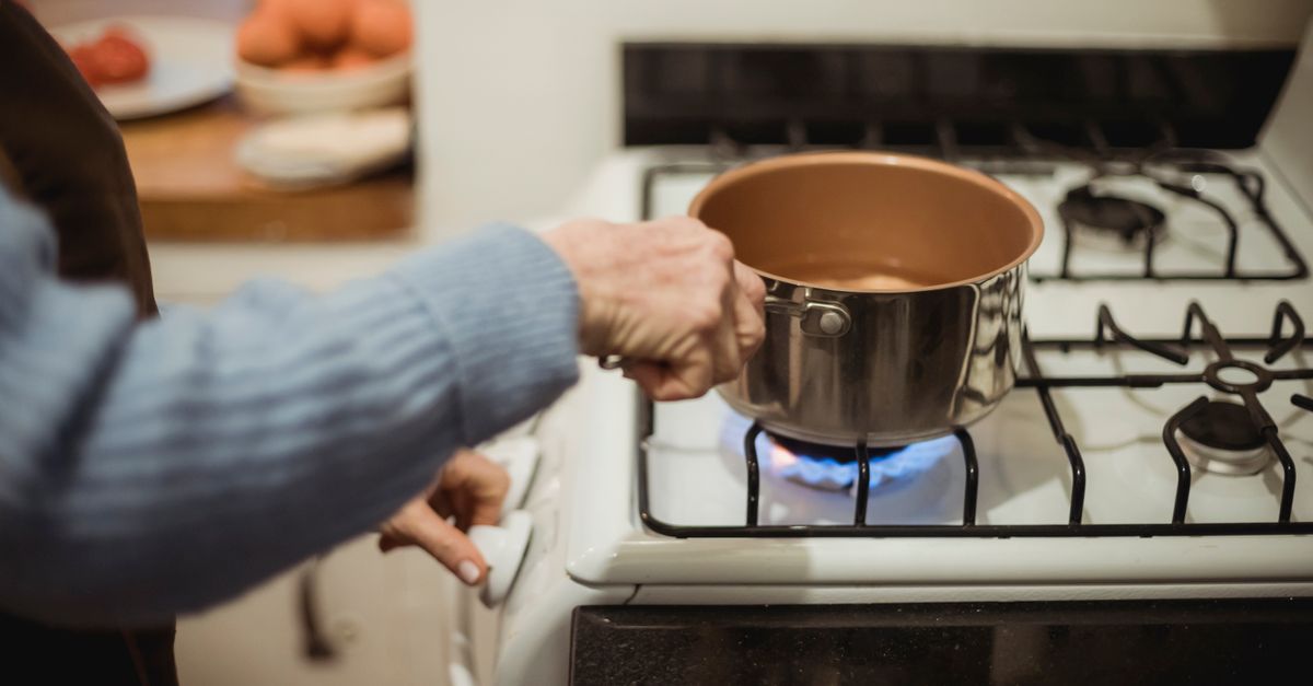 Une main tient une petite casserole en cuivre sur une flamme de gaz, sur une cuisinière domestique.