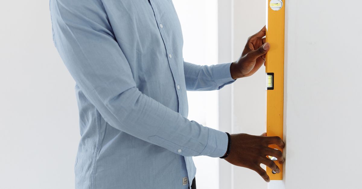 Un homme utilise un niveau à bulle jaune contre un mur blanc pour vérifier l'alignement avant une installation.