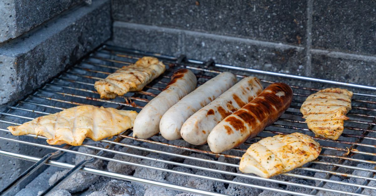 Des filets de poulet marinés grillent sur une grille de barbecue à côté de saucisses.