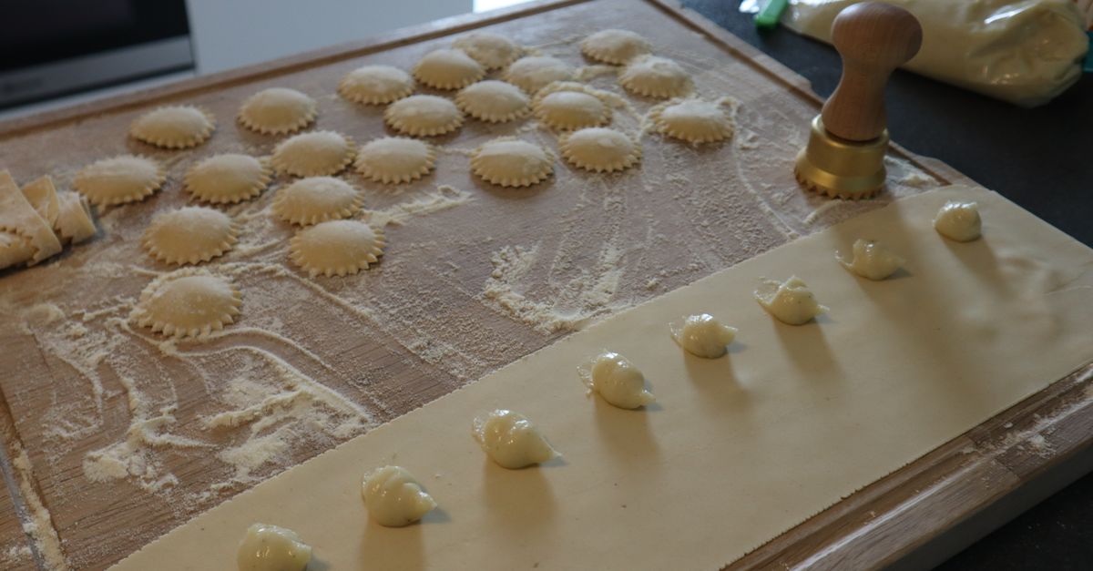 Petits raviolis façonnés à la main disposés sur une planche en bois farinée, avec un emporte-pièce à côté.