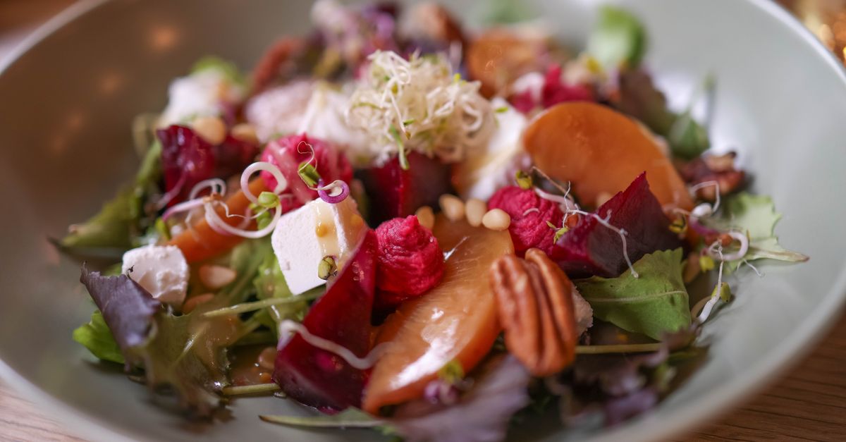 Salade composée de betteraves, chèvre frais, pignons de pin et pousses de graines dans une assiette blanche.