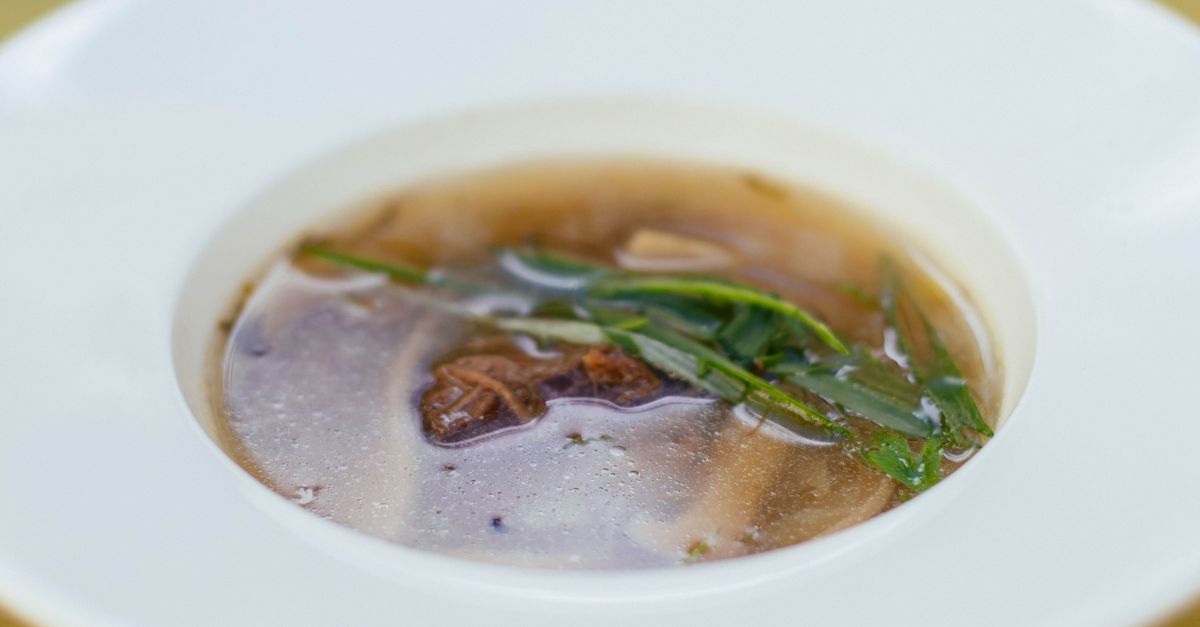 Bol blanc contenant un bouillon clair garni de ciboulette fraîche et de morceaux de viande.