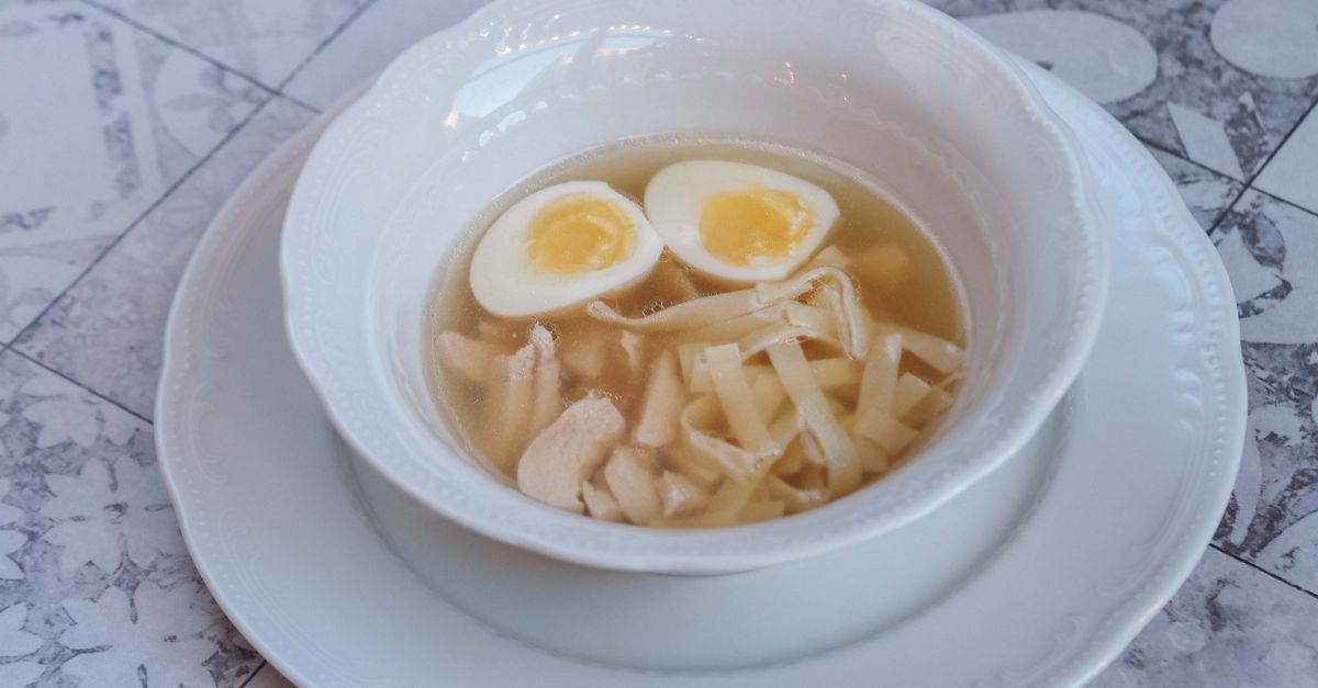 Un bol de bouillon avec des nouilles, du poulet et un œuf mollet coupé en deux au jaune coulant.