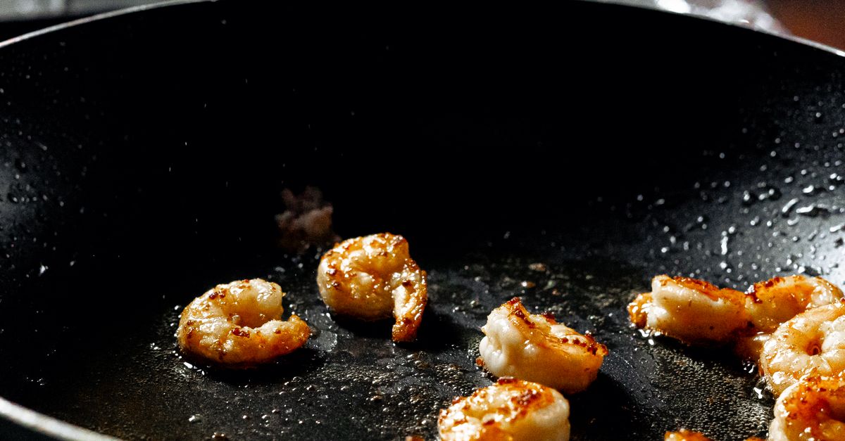 Des crevettes roses saisies dans une poêle en acier noire, avec des bords légèrement dorés.