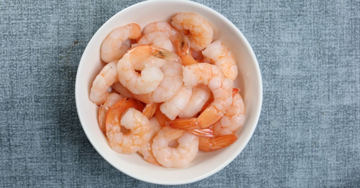 Des crevettes cuites décortiquées sont rassemblées dans un bol blanc posé sur un tissu gris.