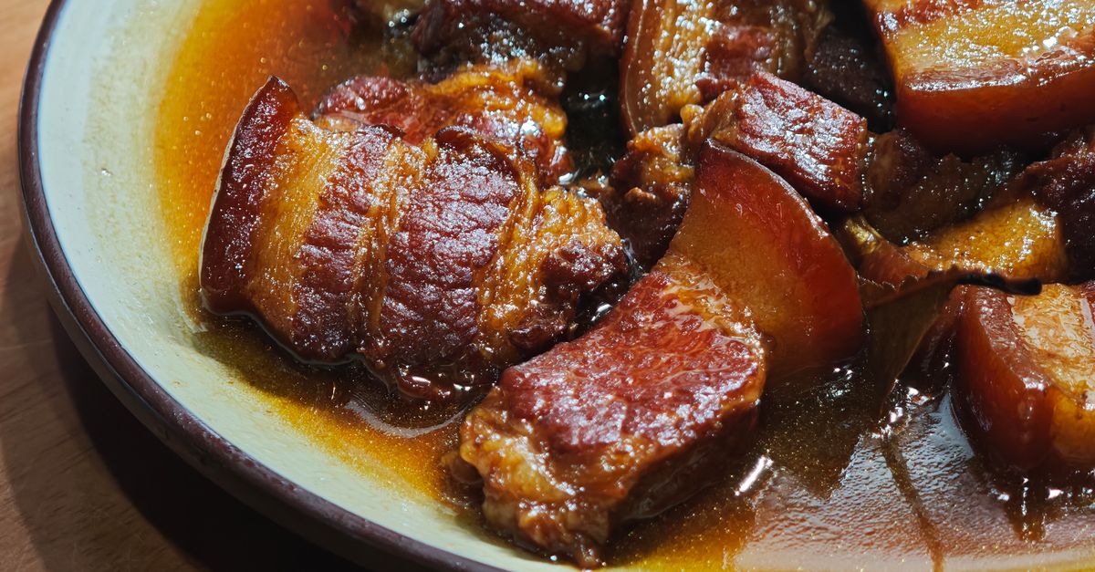 Morceaux de poitrine de porc braisée bien dorés et nappés de sauce brune dans un plat en céramique.