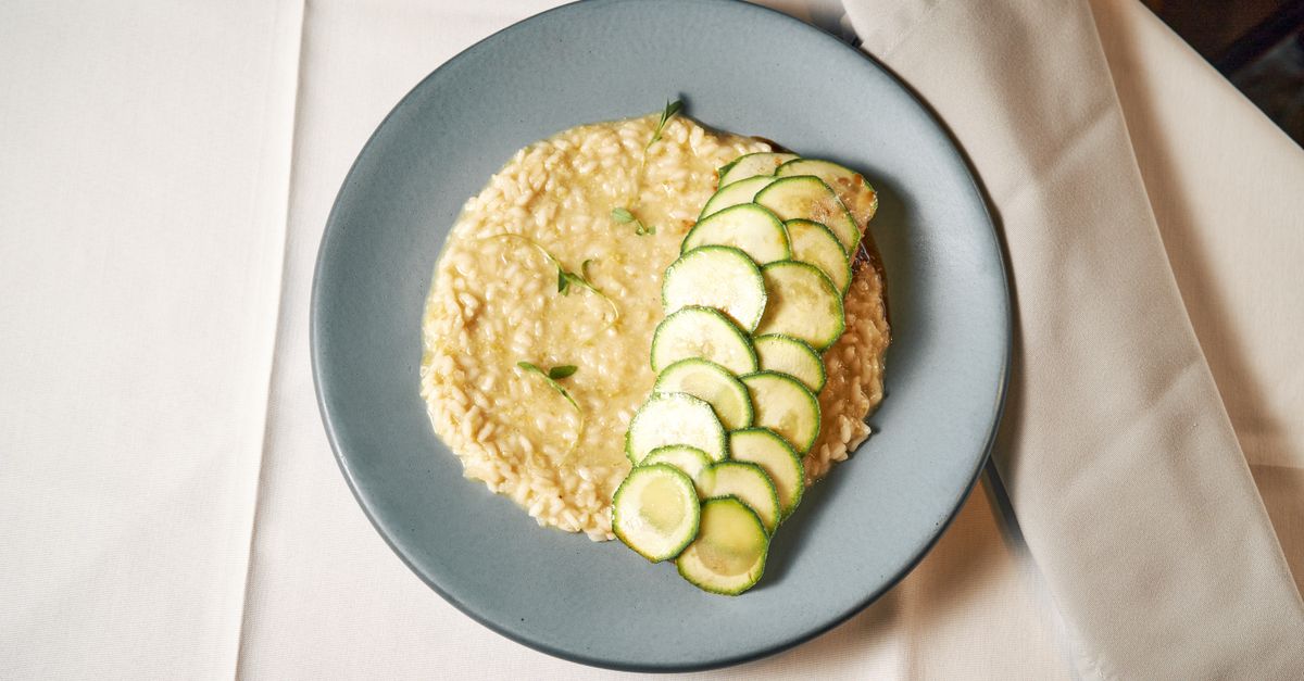 Assiette bleue vue de dessus avec un risotto crémeux à l'arborio surmonté de fines rondelles de courgette poêlées.