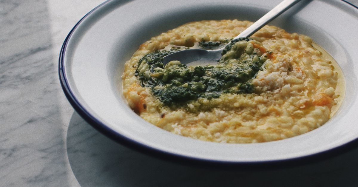 Bol de risotto crémeux garni de pesto vert et de parmesan râpé, vu de près.