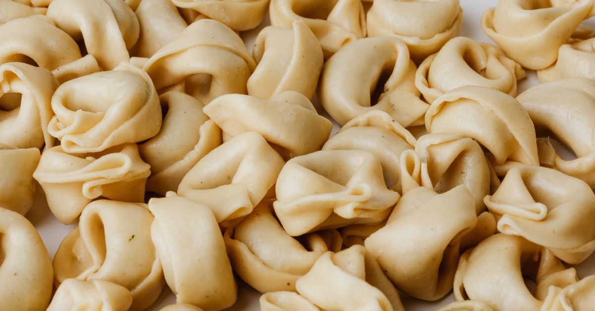Gros plan sur des tortellinis crus disposés en vrac sur une surface blanche.