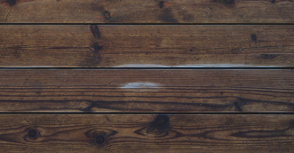 Gros plan sur des lames de parquet en bois foncé usé, montrant des joints irréguliers et des marques d'humidité entre les planches.