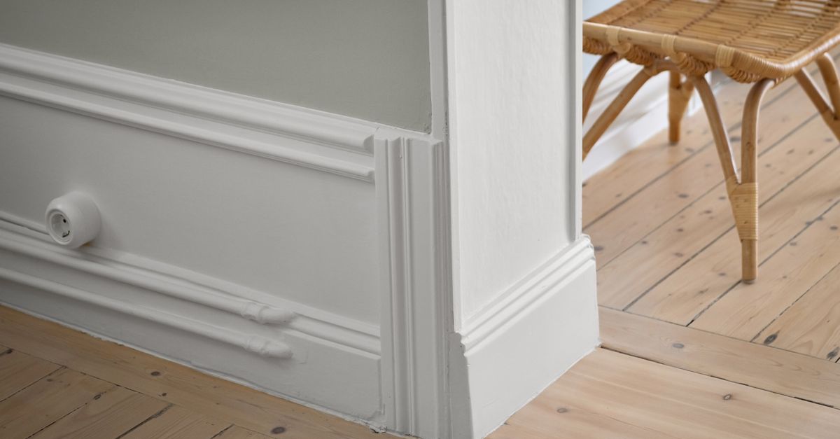 Plinthe blanche moulurée le long d'un mur, avec un parquet en bois clair visible au sol