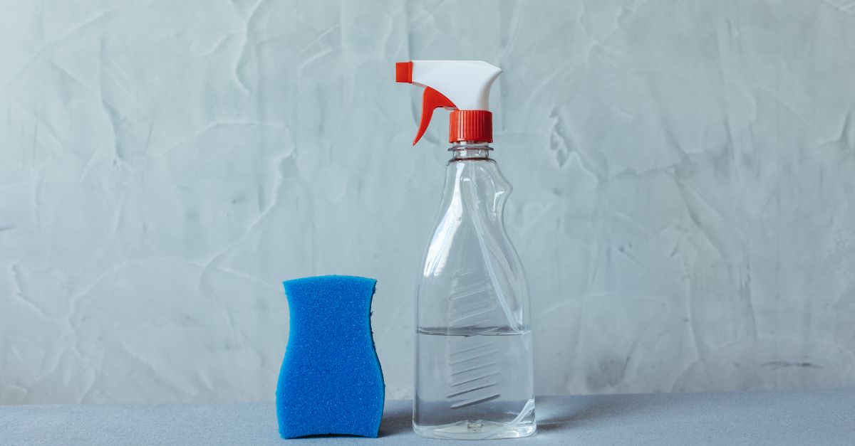 Un vaporisateur rempli d'un liquide transparent posé à côté d'une éponge bleue devant un mur clair.