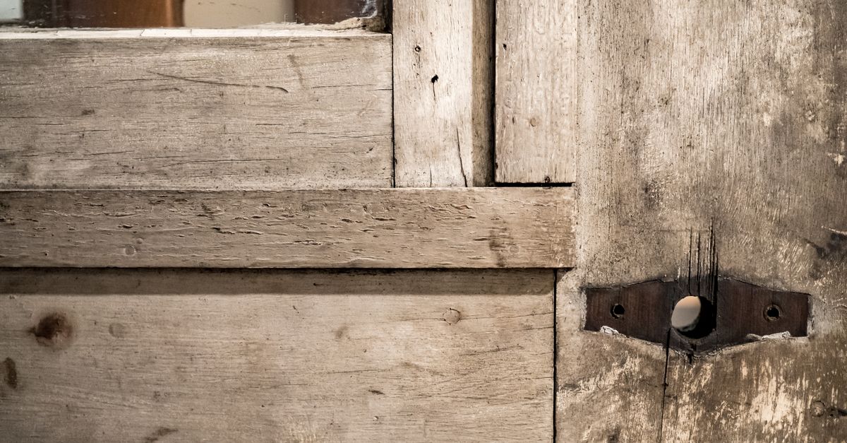 Gros plan sur une porte en bois ancienne montrant une charnière métallique fixée sur un fond de bois usé et fissuré.