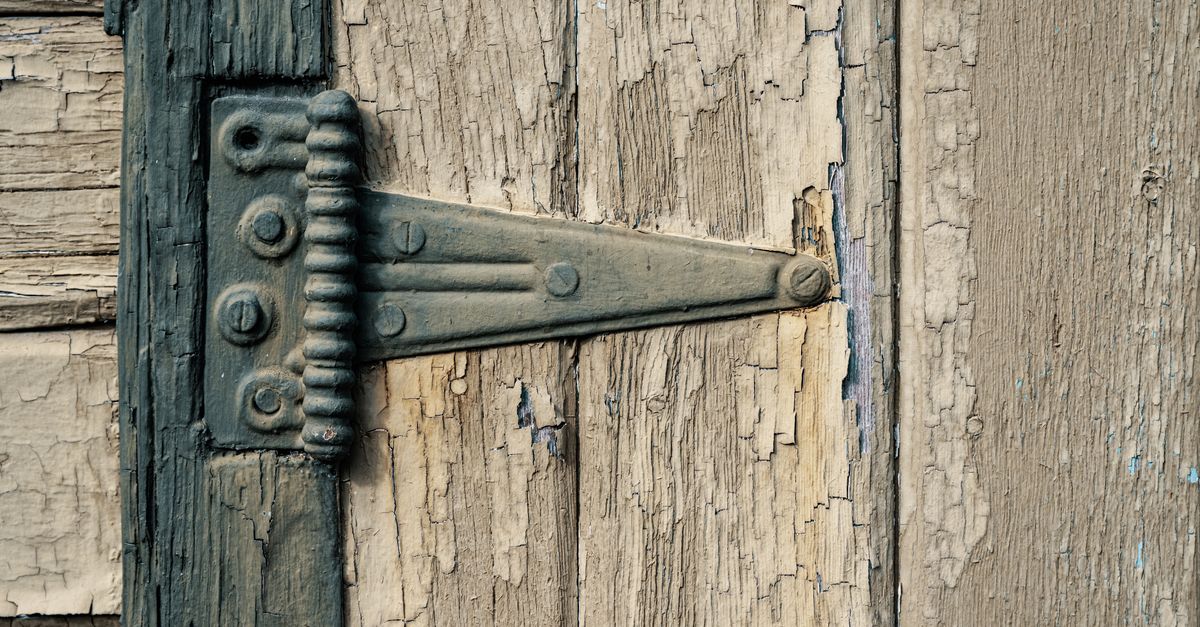 Gros plan sur une penture métallique fixée par des vis sur une porte en bois ancien à la peinture écaillée.