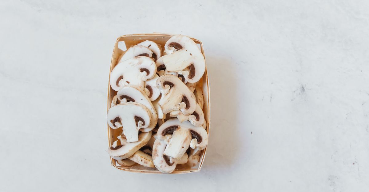 Des champignons de Paris tranchés, blancs et frais, entassés dans une barquette en carton posée sur une surface en marbre.