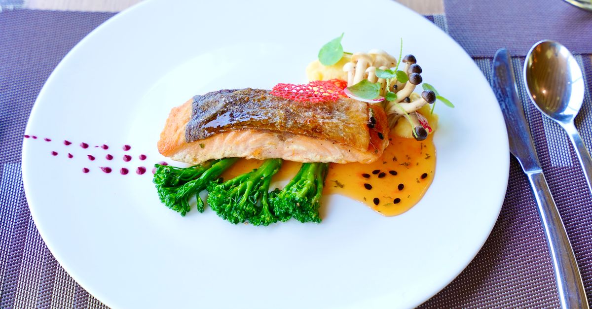Un pavé de saumon avec la peau dorée et croustillante, servi sur des brocolis avec une sauce orangée et des champignons.