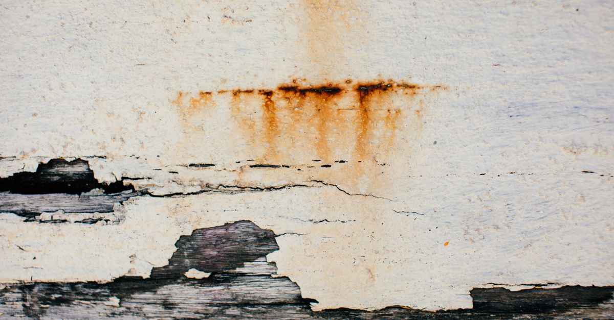 Traces de rouille coulant sur une surface peinte en blanc écaillée, rappelant des taches sur l'émail d'une baignoire.