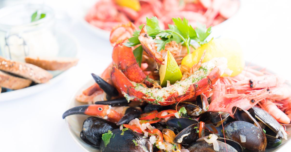 Un plateau de fruits de mer avec moules, crevettes et pinces de homard disposés sur une assiette, accompagné de citron et de pain.