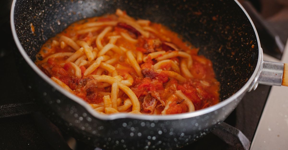 Des pâtes réchauffées dans une sauce tomate au fond d'une poêle noire sur une cuisinière.