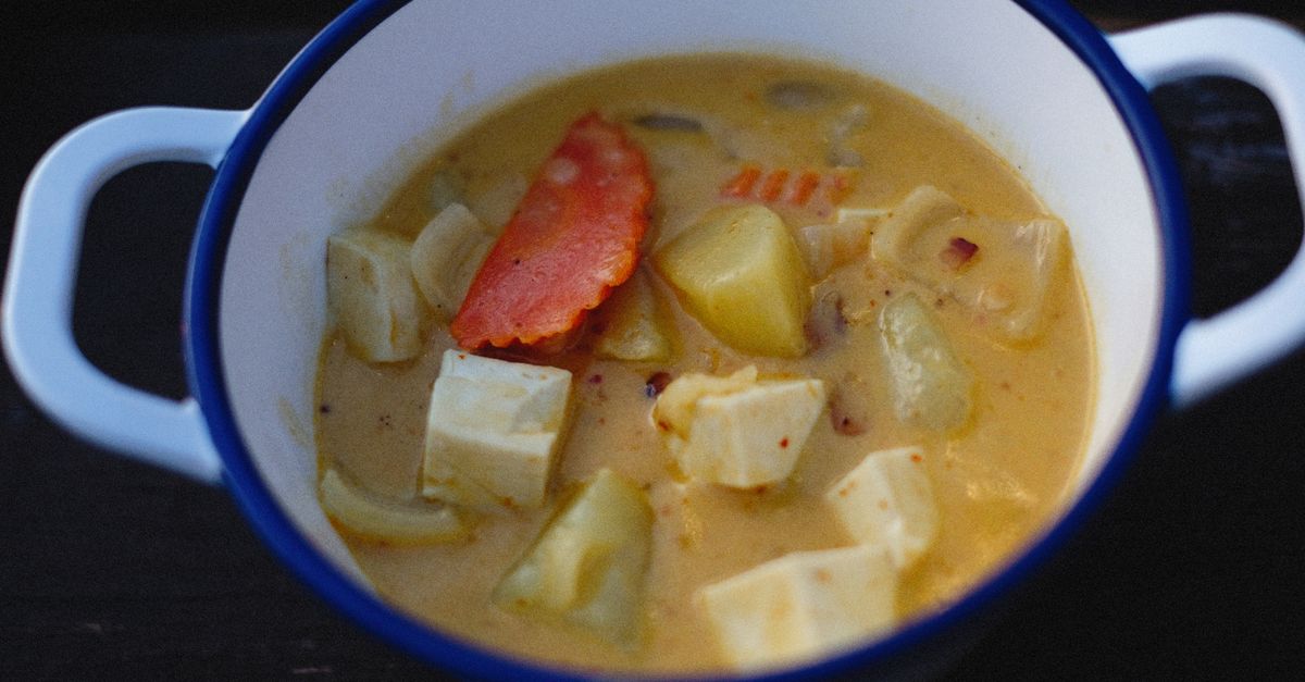 Bol en céramique blanc et bleu rempli d'une soupe crémeuse au curry avec des morceaux de pomme de terre, de tofu et de carotte.
