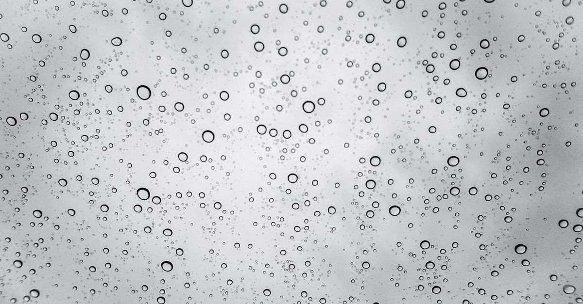 Gros plan sur une vitre couverte de multiples gouttes d'eau en noir et blanc.