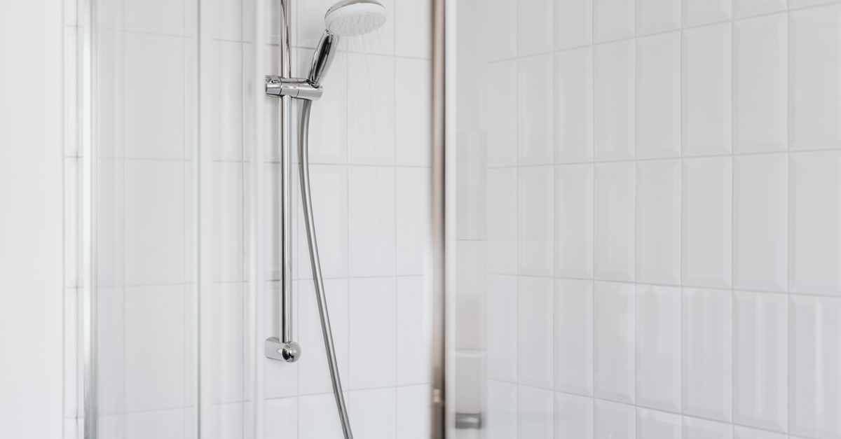 Douche vitrée avec une pomme de douche chromée et des carreaux blancs propres.