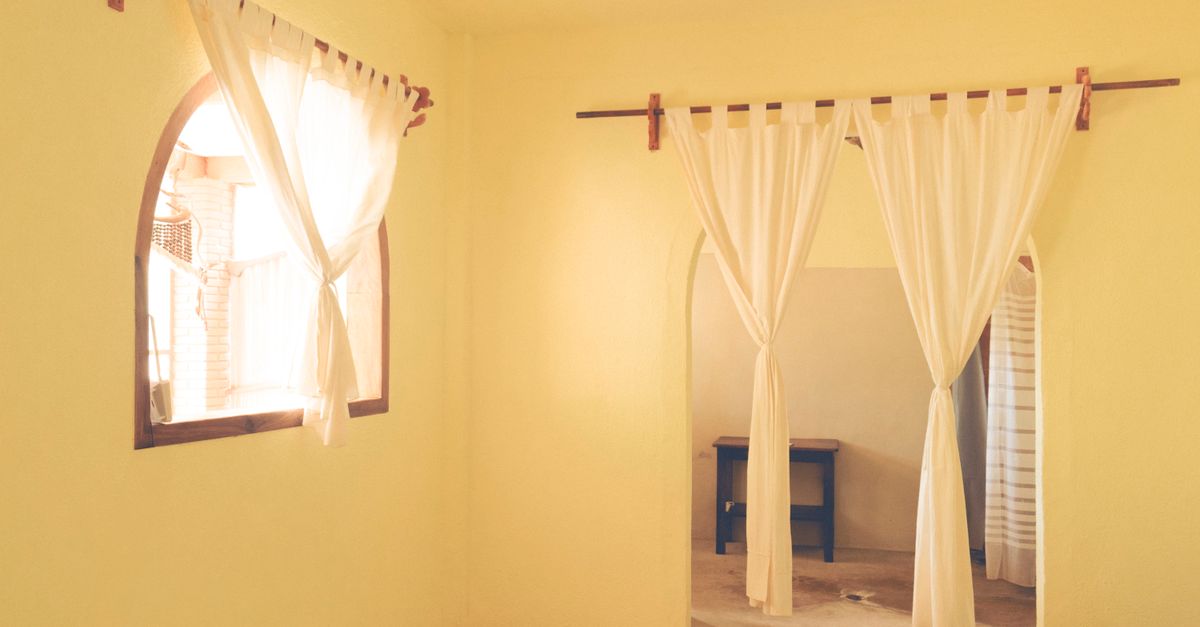 Un voile blanc léger suspendu à une tringle en bois montée sans perçage devant une fenêtre cintrée et une ouverture intérieure.
