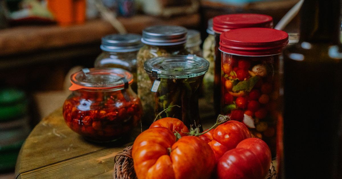 Bocaux de conserves de tomates et légumes marinés posés sur une table en bois à côté de tomates fraîches.