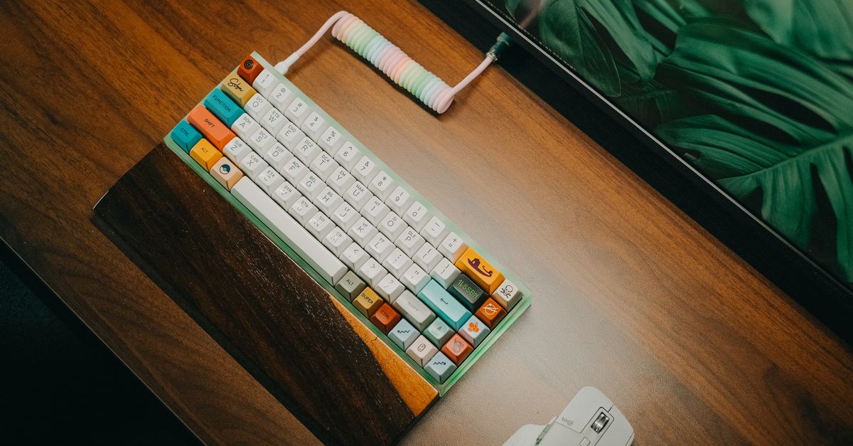Un clavier mécanique coloré posé sur un support en bois, vu de dessus sur un bureau en bois.