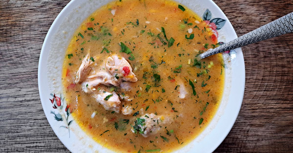 Une assiette creuse remplie de bouillon de poisson doré garni de morceaux de poisson et d'herbes fraîches, avec une cuillère posée dedans.