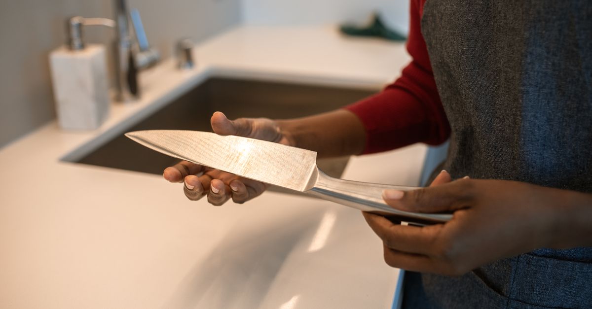 Une personne tient un couteau de chef en acier inoxydable près d'un évier de cuisine, semblant l'examiner ou le nettoyer.