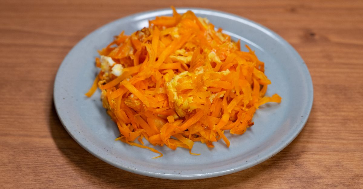 Une assiette de carottes râpées bien orangées avec des morceaux d'œuf, posée sur une table en bois.