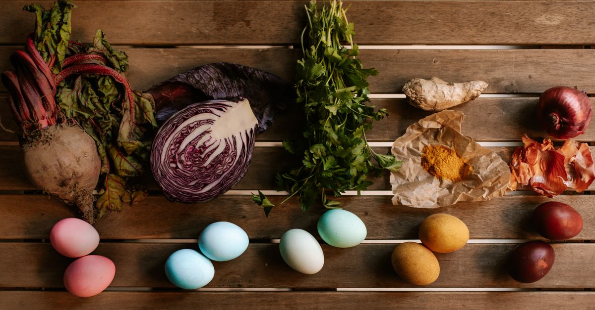 Une betterave crue entière avec ses fanes posée parmi d'autres légumes sur une table en bois