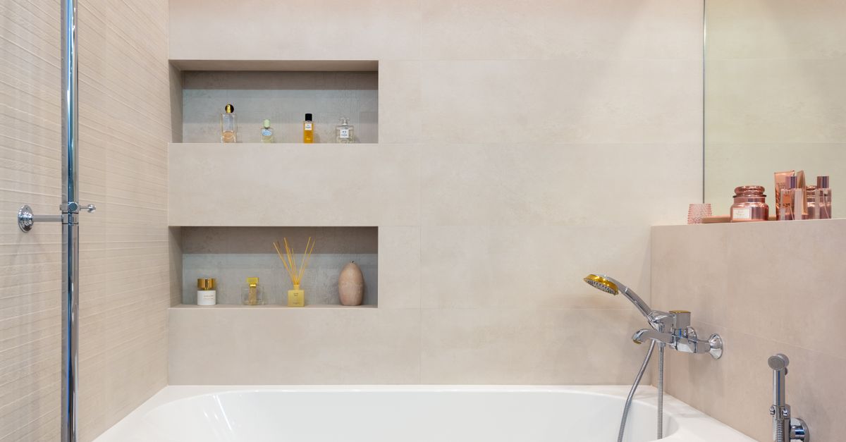 Niches murales encastrées au-dessus d'une baignoire avec flacons de parfum et bougies décoratives disposés sur les étagères creusées dans le mur carrelé.