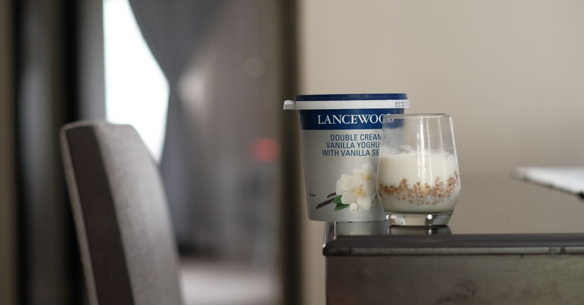 Un pot de yaourt à la vanille de marque Lancewood posé à côté d'un verre rempli de yaourt versé, sur une table.