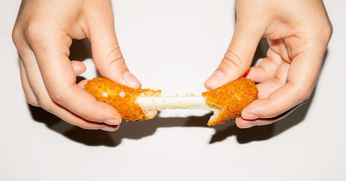 Un bâton de mozzarella pané tenu à deux mains, tiré en deux pour révéler le fromage fondant qui s'étire au centre.