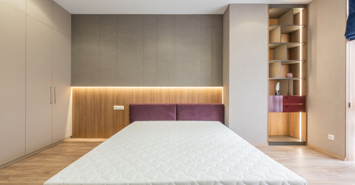 Chambre avec tête de lit capitonnée bordeaux et étagère murale en bois intégrée avec éclairage indirect au-dessus du lit.